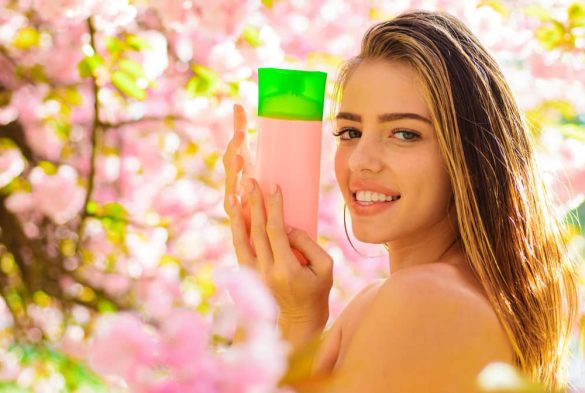 Femme souriante tenant un flacon de shampoing sans sulfate devant des fleurs de cerisier roses.